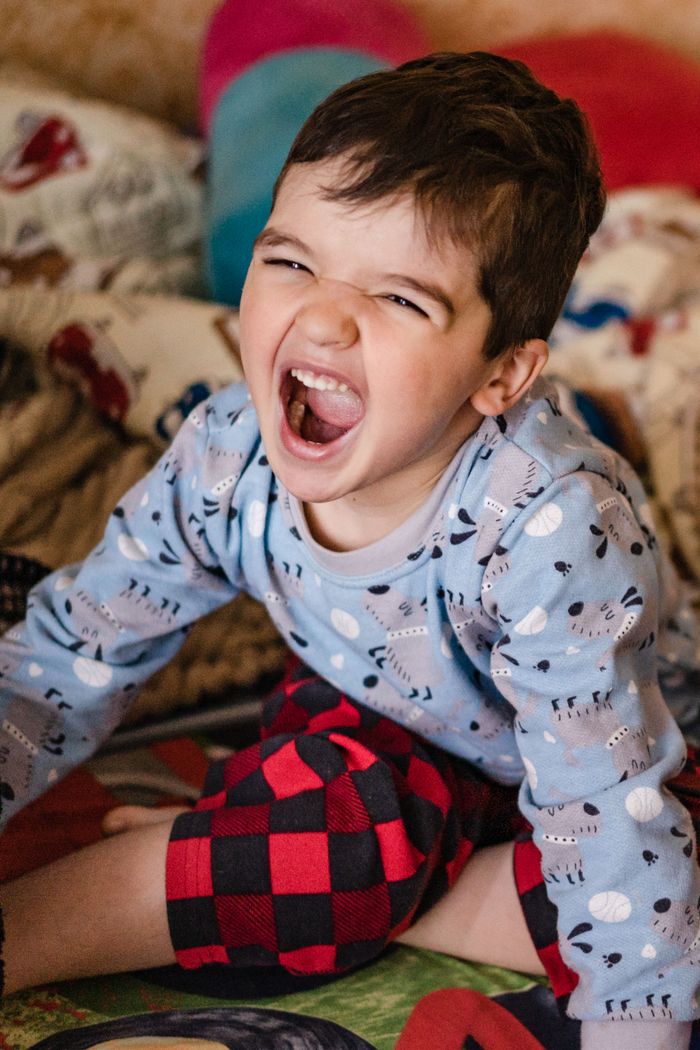 Young boy in playful mood wearing pajamas, sitting indoors and expressing excitement.
